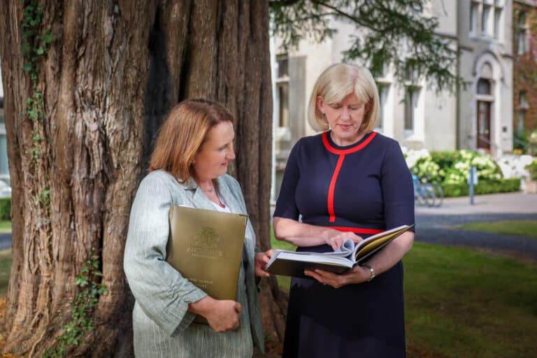 Two ladies reviewing archive books under a tree at Cahernane